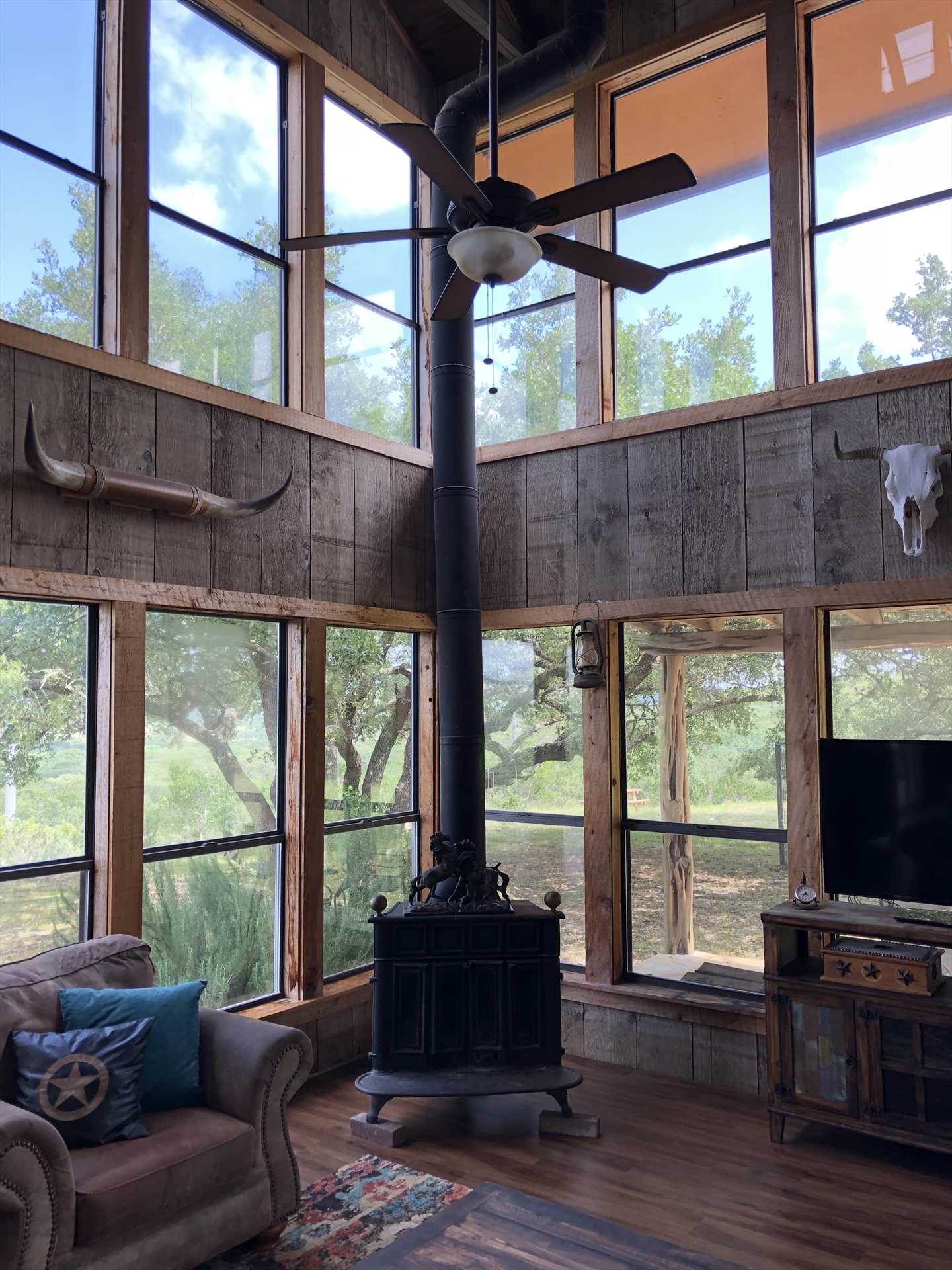                                                 The spacious living area at the Bluff House offers breathtaking two-story windowed views of the Hill Country, along with the decorative charm of a wood stove (which is inoperable at this time).